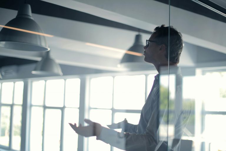 Startseite Fachbeitraege Business professional giving a presentation in a modern office setting through glass.