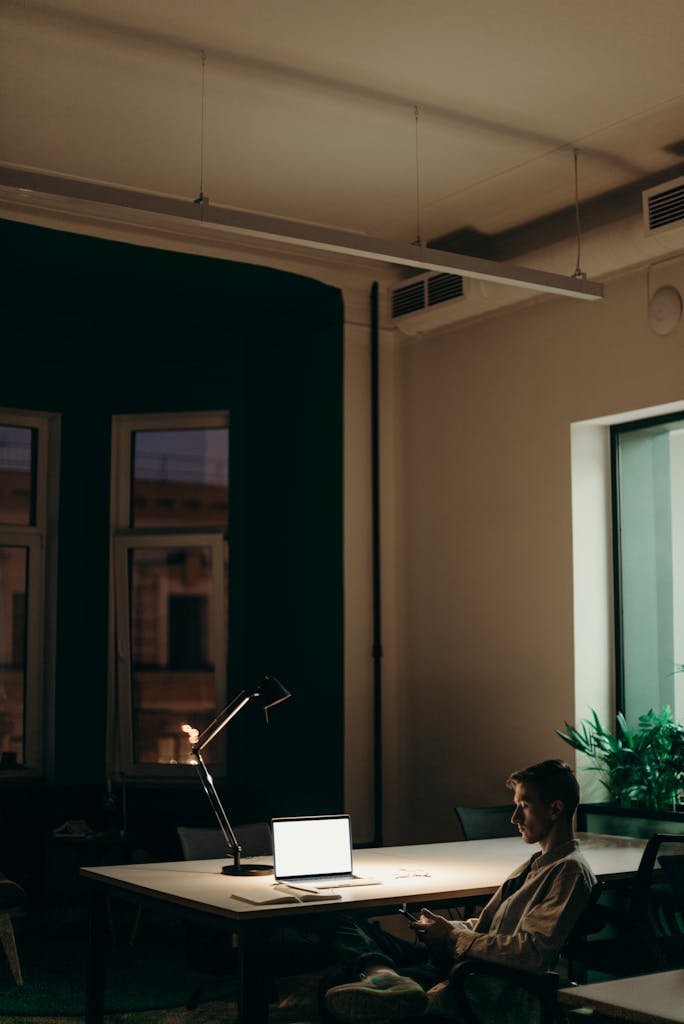 Kunden Krise Man working late in an office using a laptop under a desk lamp, showcasing dedication and focus.